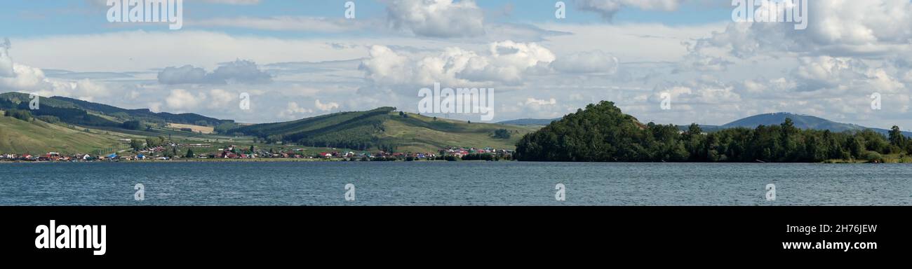 Das Dorf Parnaya liegt am Ufer des Großen Sees auf dem Hintergrund der Waldhügel an einem Sommertag. Region Krasnojarsk. Russland. Stockfoto