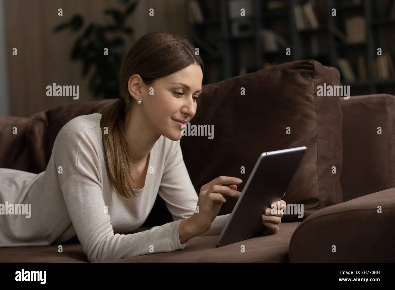 Lächelnde attraktive Frau, die sich alleine auf dem Sofa mit digitalem Tablet entspannt Stockfoto