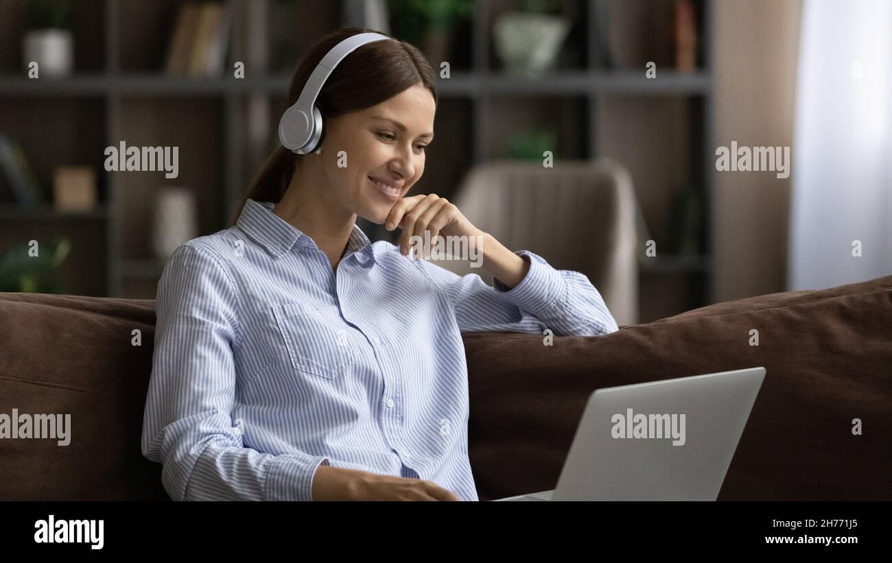Frau mit Kopfhörern verwendet einen Laptop, um sich einen Film anzusehen oder ein Webinar zu Bildung zu machen Stockfoto