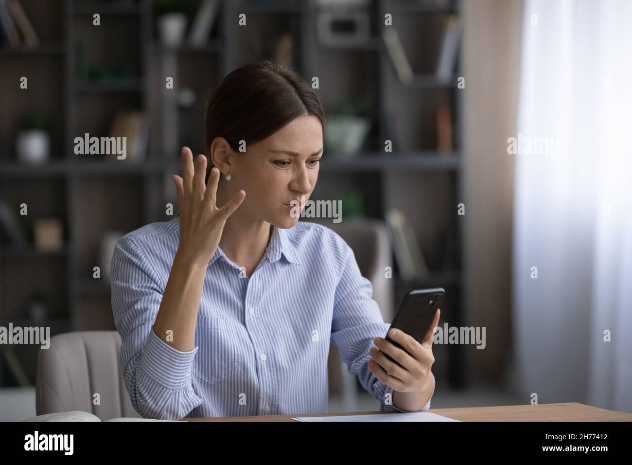 Geschäftsfrau, die Probleme mit dem Handy hat, fühlt sich genervt, am Schreibtisch zu sitzen Stockfoto