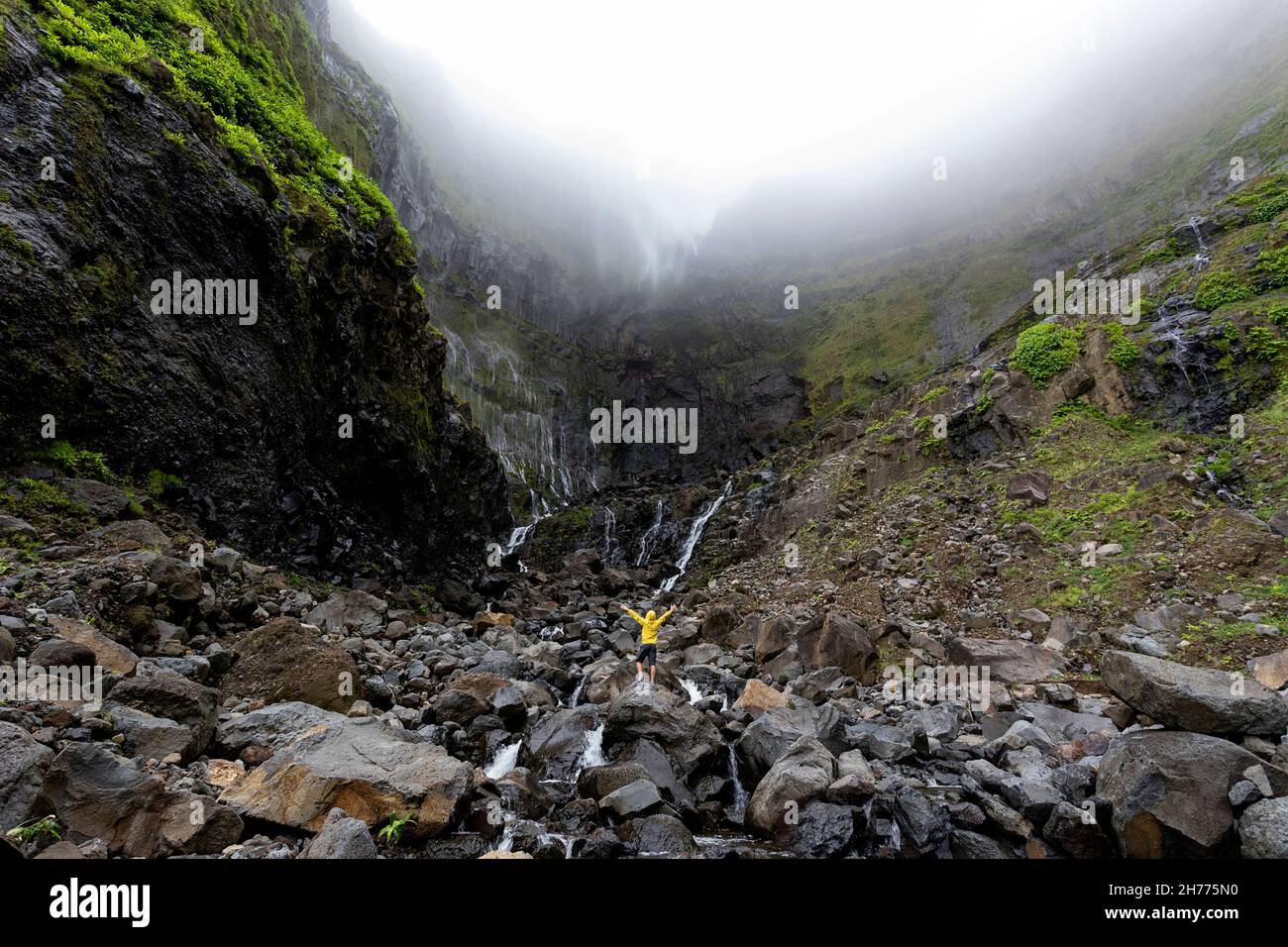 Junge mit gelber Jacke, der die Hände beim Ribeira grande Wasserfall hebt. Flores, Azoren, Portugal Stockfoto