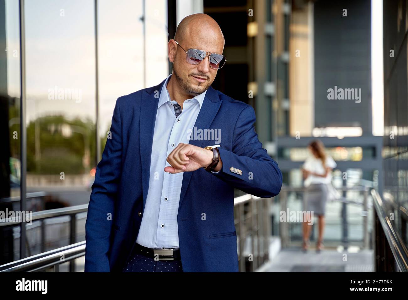 Selbstbewusster Geschäftsmann, in formeller Kleidung und Brille, stehend und auf seine Uhr schauend, während er auf der Straße steht. Hohe Qualität Stockfoto