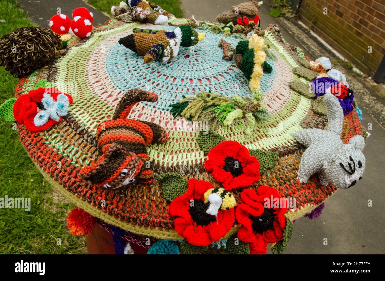 Eine Häkelauflage auf einer Royal Mail-Säulenbox mit Blumen und Tieren. Bürgersteig in Basingstoke, Hampshire. Stockfoto