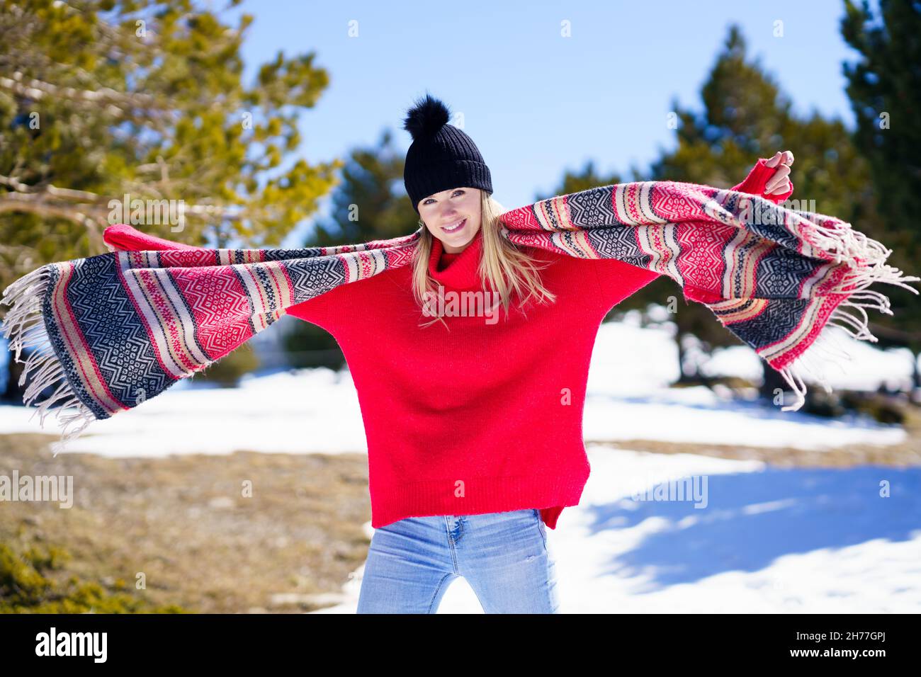 Junge glückliche junge blonde Frau winkt ihren Schal im Wind in einem Wald in den verschneiten Bergen. Stockfoto