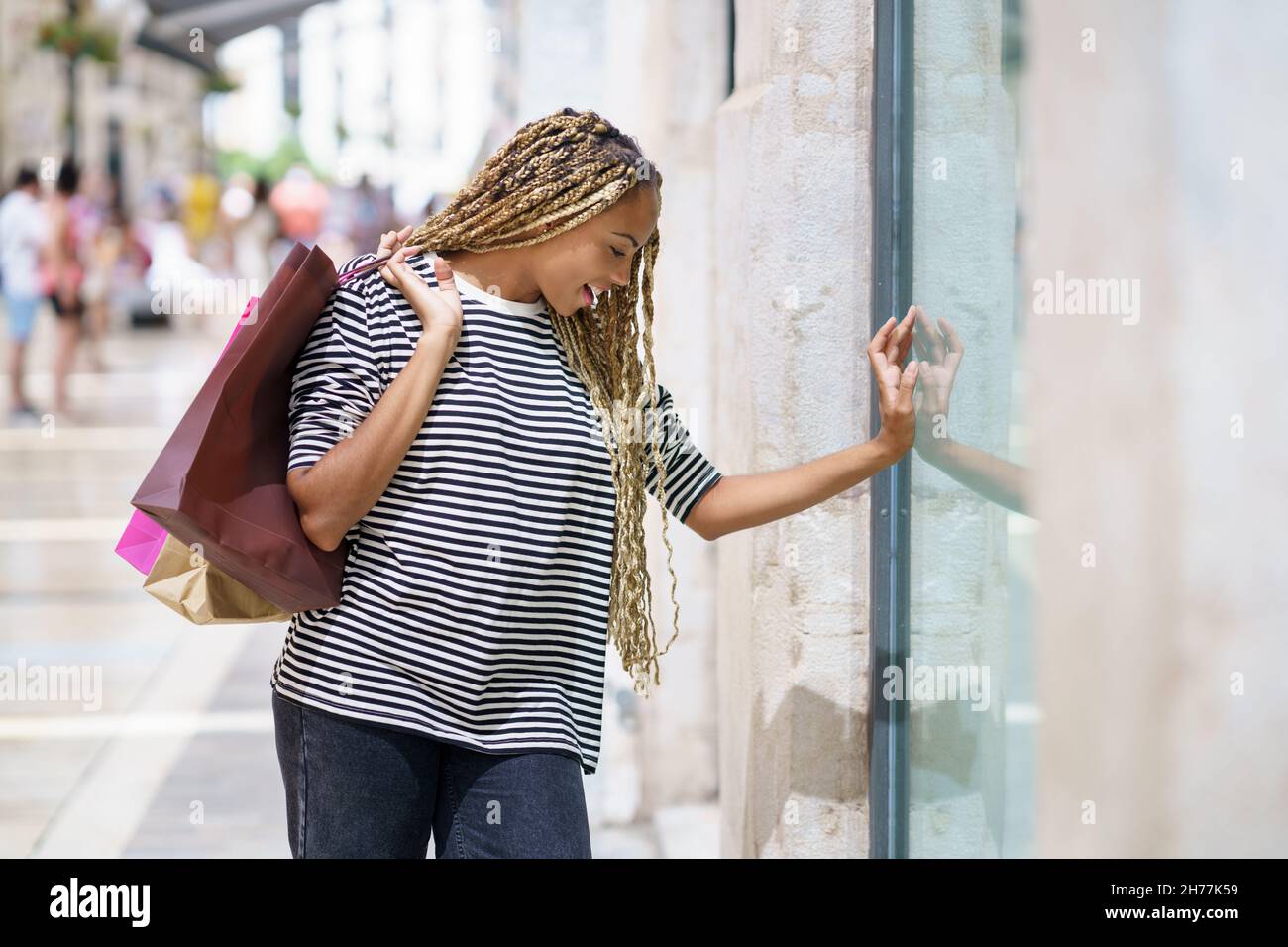 Schwarze Frau vor einem Schaufenster in einer Einkaufsstraße. Weibchen mit afrikanischen Zöpfen. Stockfoto