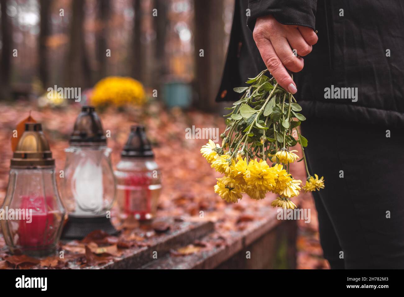 Respekt vor toten Menschen. Trauernde Frau, die Blumen in den Händen hält und am Grab auf dem Friedhof steht. Stockfoto