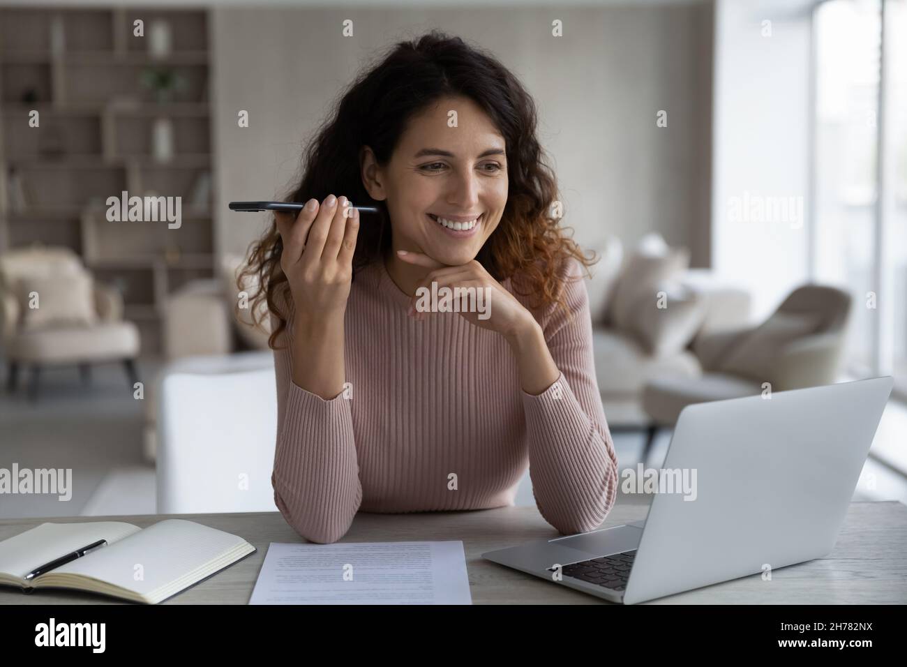 Lächelnde, zufriedene Geschäftsfrau, die das Smartphone hält und die Sprachnachricht hört Stockfoto