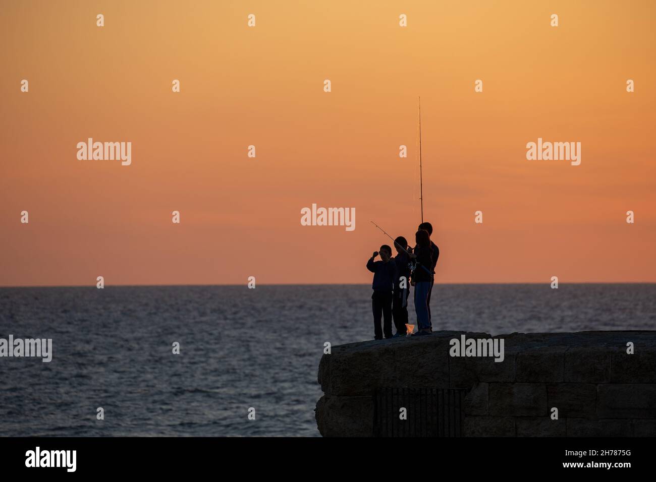 Mediterraner Sonnenuntergang fotografiert in Acre Israel Silhouette von lokalen Jungen Angeln Stockfoto