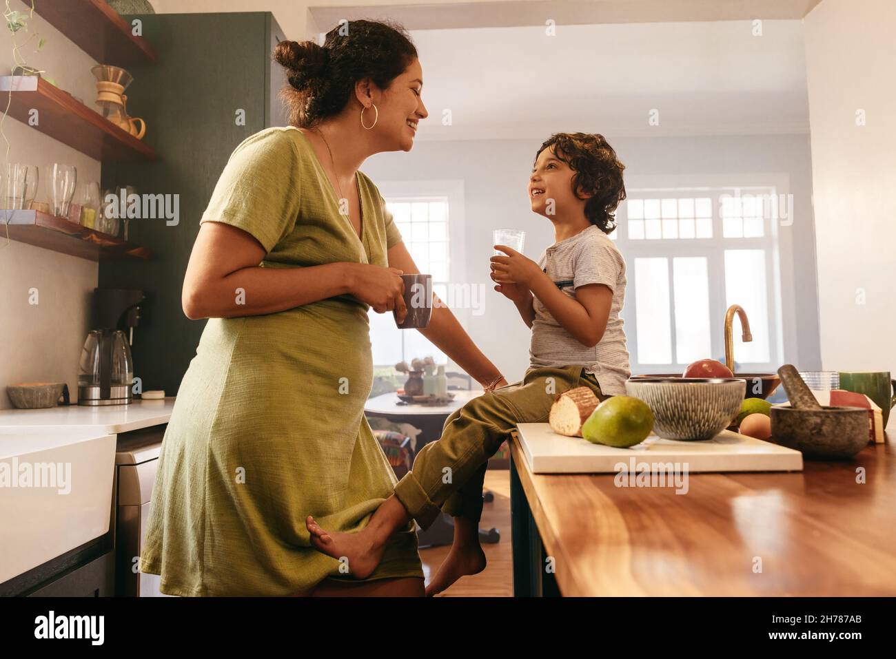Glückliche Mutter und Sohn lächeln sich liebevoll an. Mutter und Sohn trinken ihre Morgengetränke in der Küche zu Hause. Fürsorgliche einzelne mothe Stockfoto
