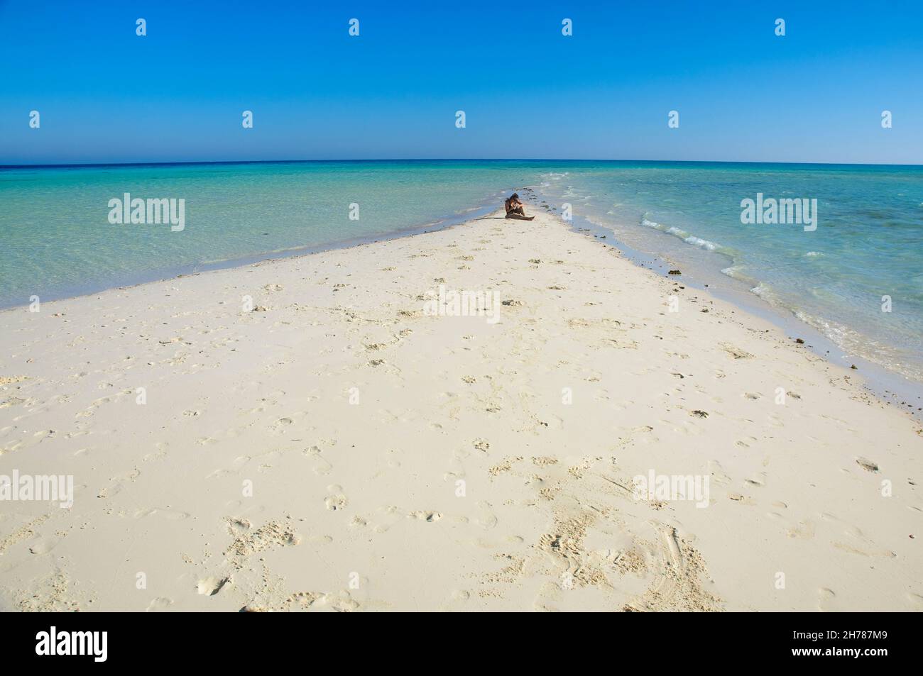 Ägypten, Sinai Desert Peninsula , Ras Mohammed, Frau in ihren Zwanzigern sitzt allein auf einem langen Stück verlassenen Strand endlosen Horizont von Ozean und Himmel in Stockfoto