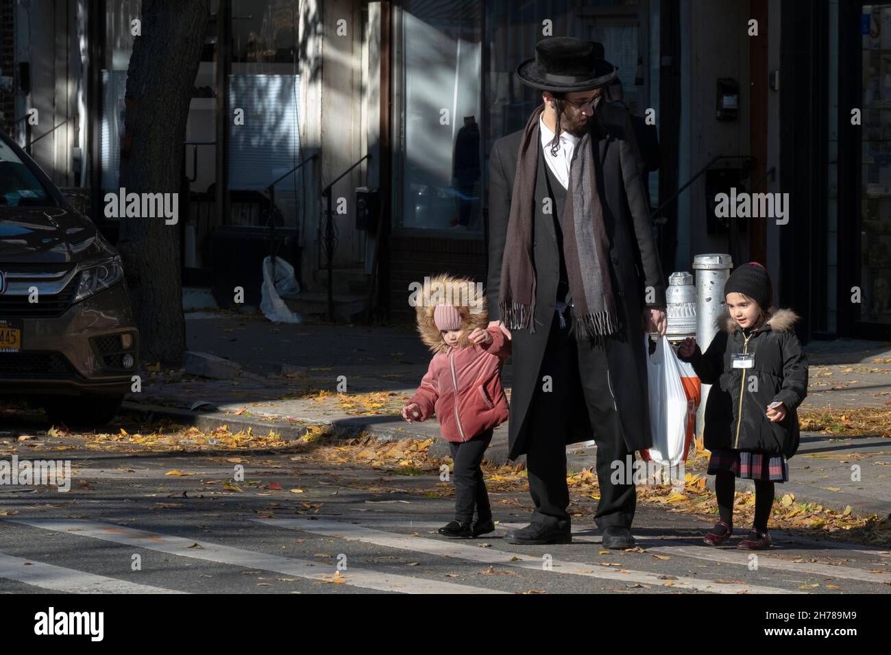 Ein orthodoxer jüdischer Vater überquert die Straße aufmerksam auf seine Kinder. Auf der Lee Avenue in Williamsburg, Brooklyn, New York. Stockfoto