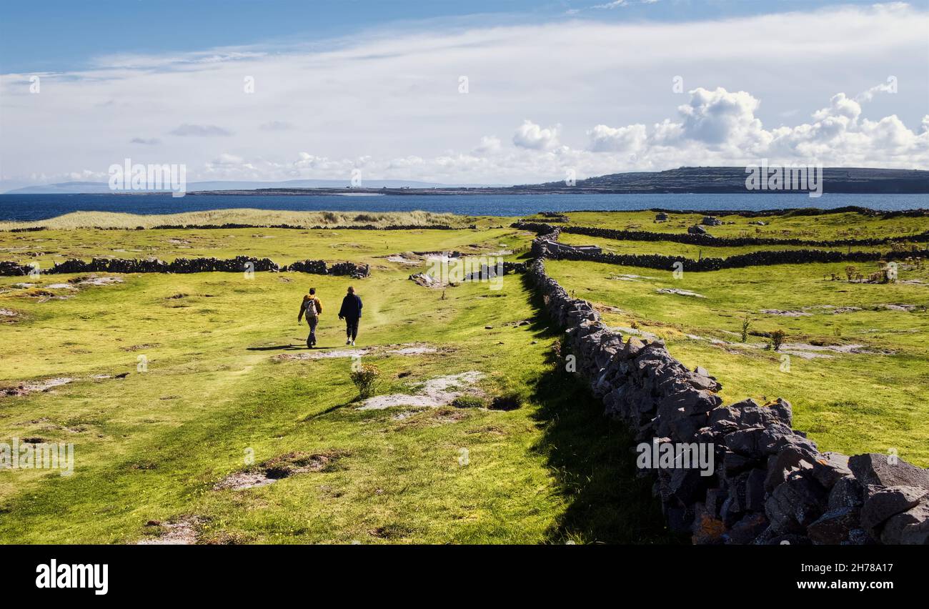 Wunderschöne Landschaft mit grünen Feldern und Steinmauern mit Menschen, die an den Aran-Inseln im County Galway, Irland, vorbeikommen Stockfoto