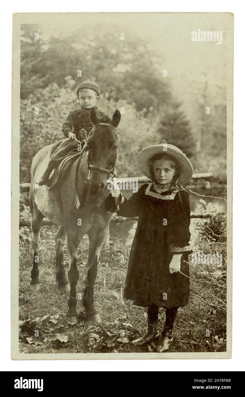 Originalpostkarte aus dem frühen 20. Jahrhundert mit einem kleinen Jungen, der auf einem Pferd sitzt, dessen Schwester die Zügel in der Hand hält, Llandygwydd, Cardiganshire, Wales, Großbritannien, um 1909 Stockfoto