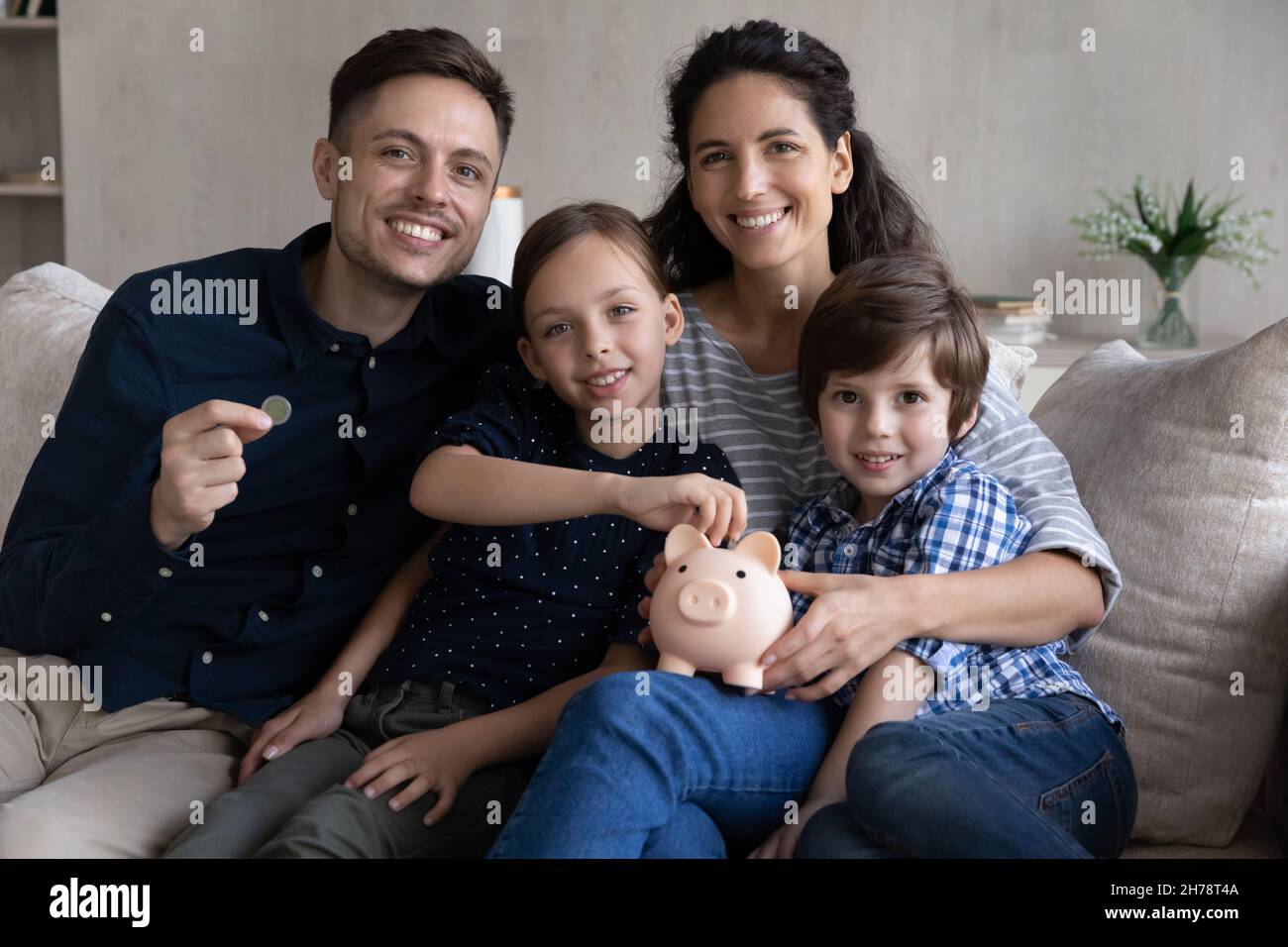 Schönes Paar und Kinder sitzen auf dem Sofa mit Sparschwein Stockfoto