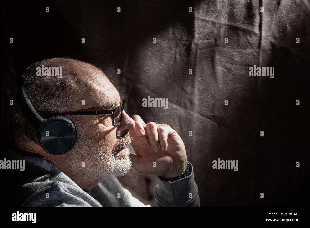 Flaches Porträt eines grauhaarigen Mannes, der über Kopfhörer Musik hört Stockfoto