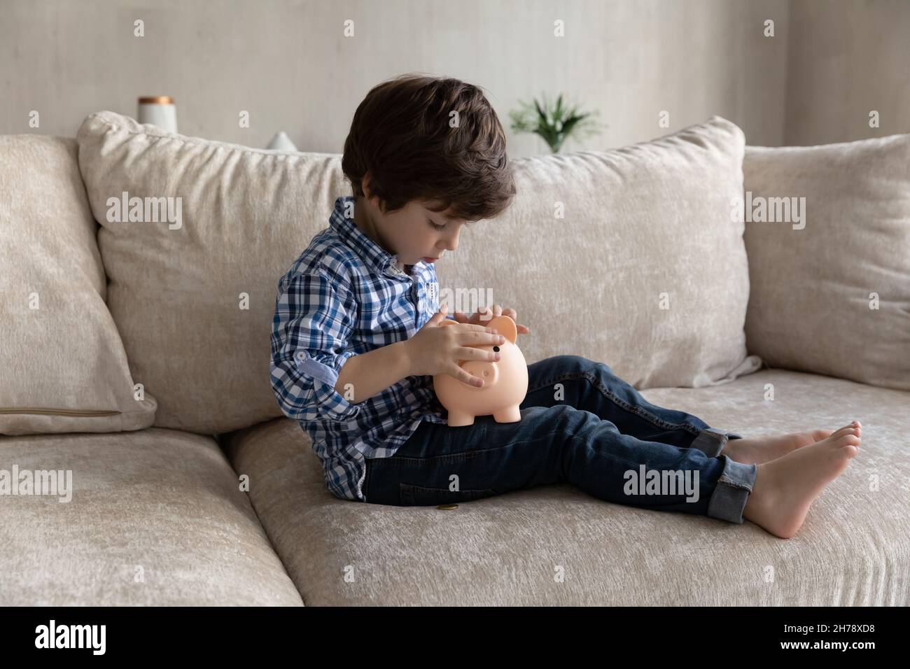 Vorschuljunge sitzt auf dem Sofa Werfen Sie Münzen in Sparschwein Stockfoto