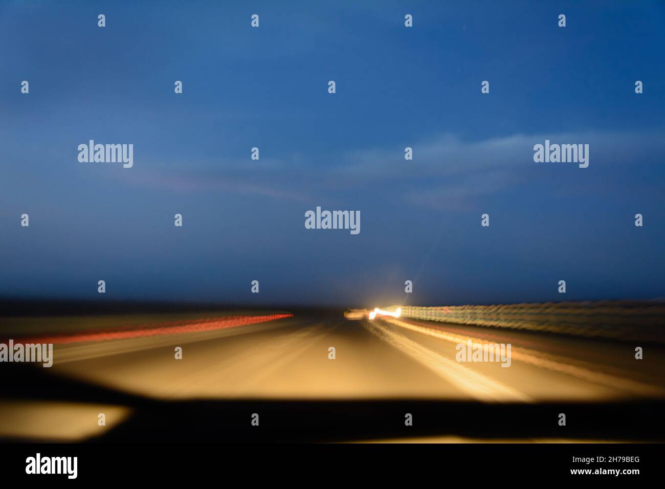 Lange Belichtung auf der Straße mit Lichtgeschwindigkeit im Auto bei Sonnenuntergang mit bewölktem Himmel. Licht von der Straße und Autos vor dem Scheibenwischer. blu Stockfoto