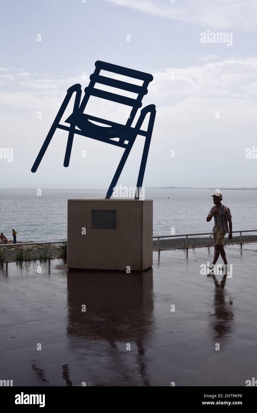 Regentag auf der Promenade des Anglais mit Mann, der am Big Blue Chair vorbeiläuft Skulptur von Sabine Geraudie Nice Alpes-Maritimes Frankreich Stockfoto