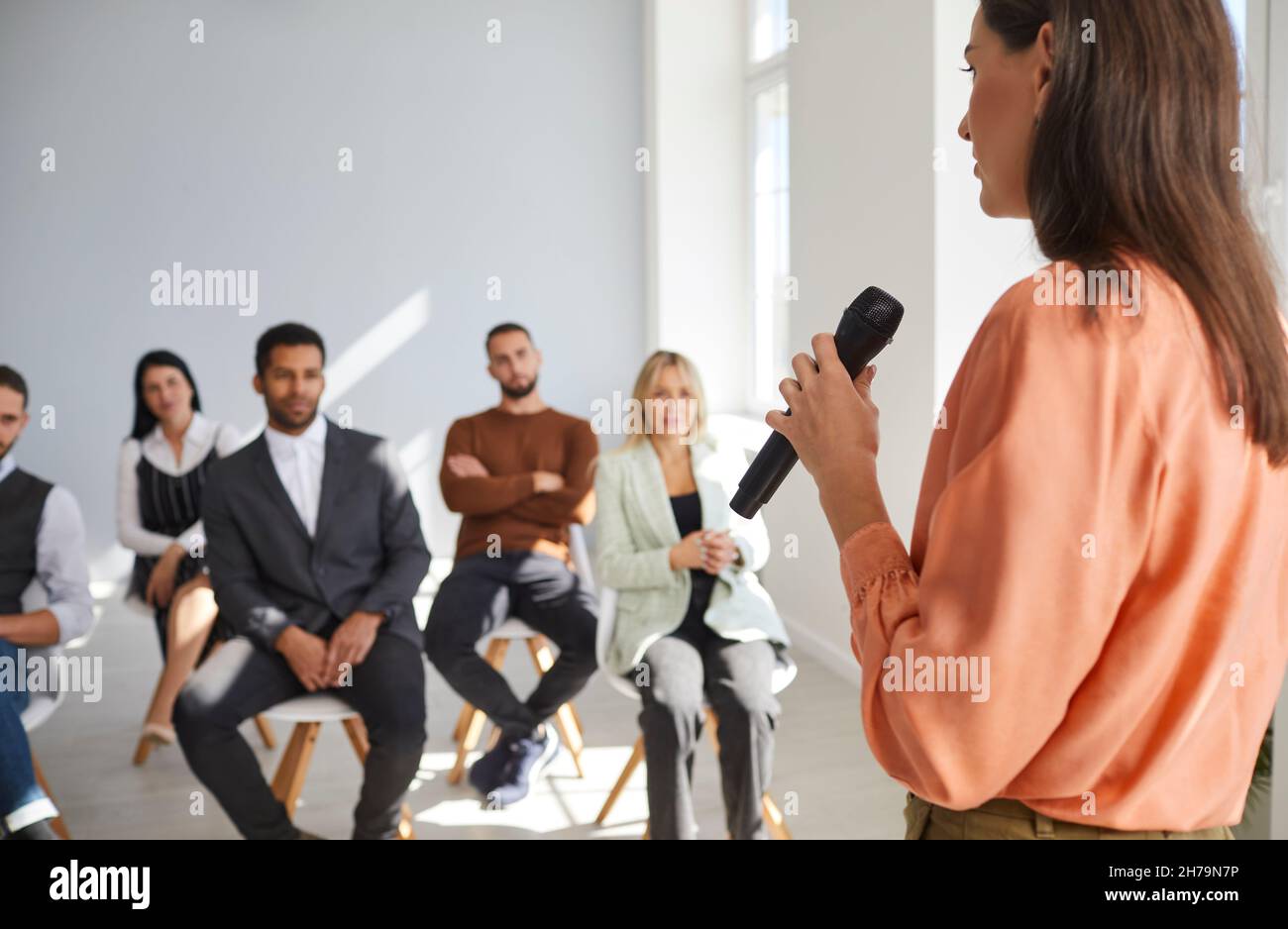 Sprecherin mit Mikrofon in der Hand spricht vor einer kleinen Gruppe von Geschäftsleuten. Stockfoto