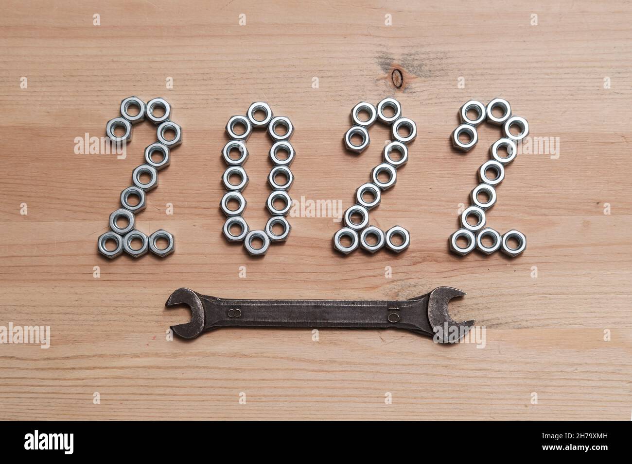 Die Zahlen des neuen Jahres 2022 sind mit Metallmuttern auf einem Holztisch ausgekleidet und mit einem Schraubenschlüssel hervorgehoben. Draufsicht. Stockfoto