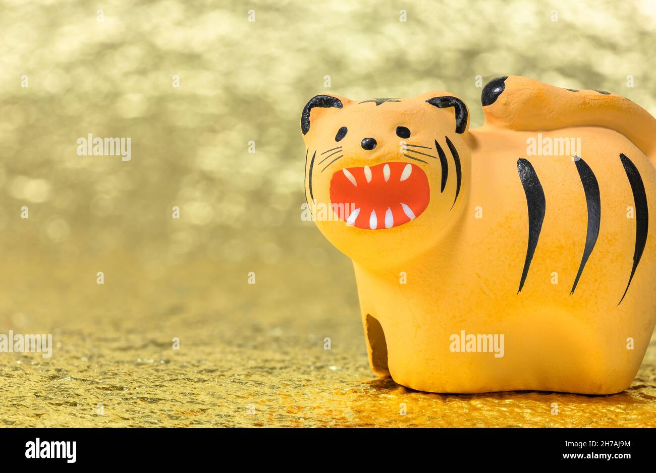 Japanische Neujahrskarte mit einer handgefertigten Figur eines brüllenden Tigers für das Jahr 2022 gegen eine glitzernde goldene Ba Stockfoto