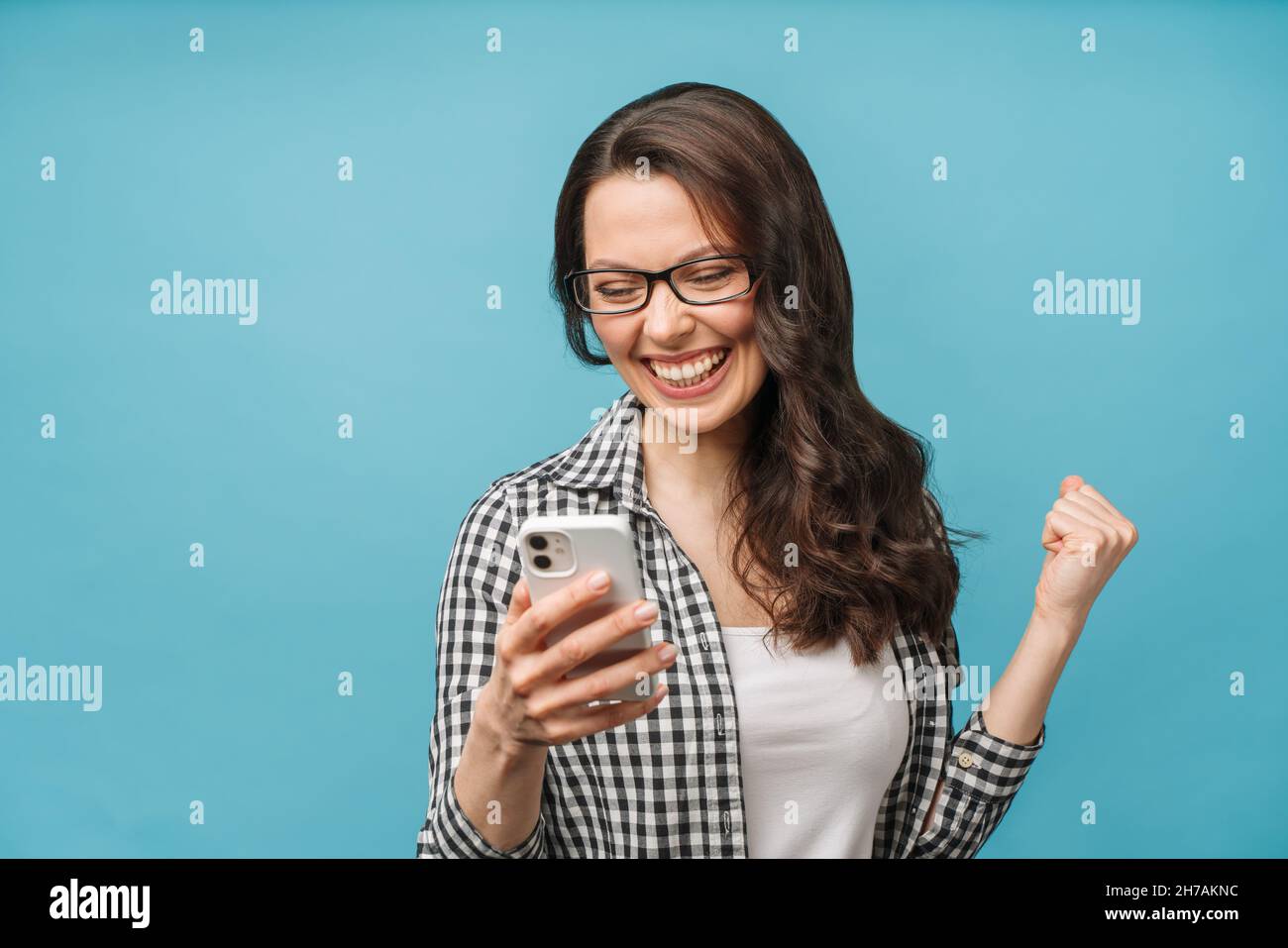 Aufgeregt glücklich Brünette Blick auf Telefonbildschirm, feiert Online-Sieg, überglücklich junge Frau schreiend vor Freude, hält Smartphone, gut lesen Stockfoto