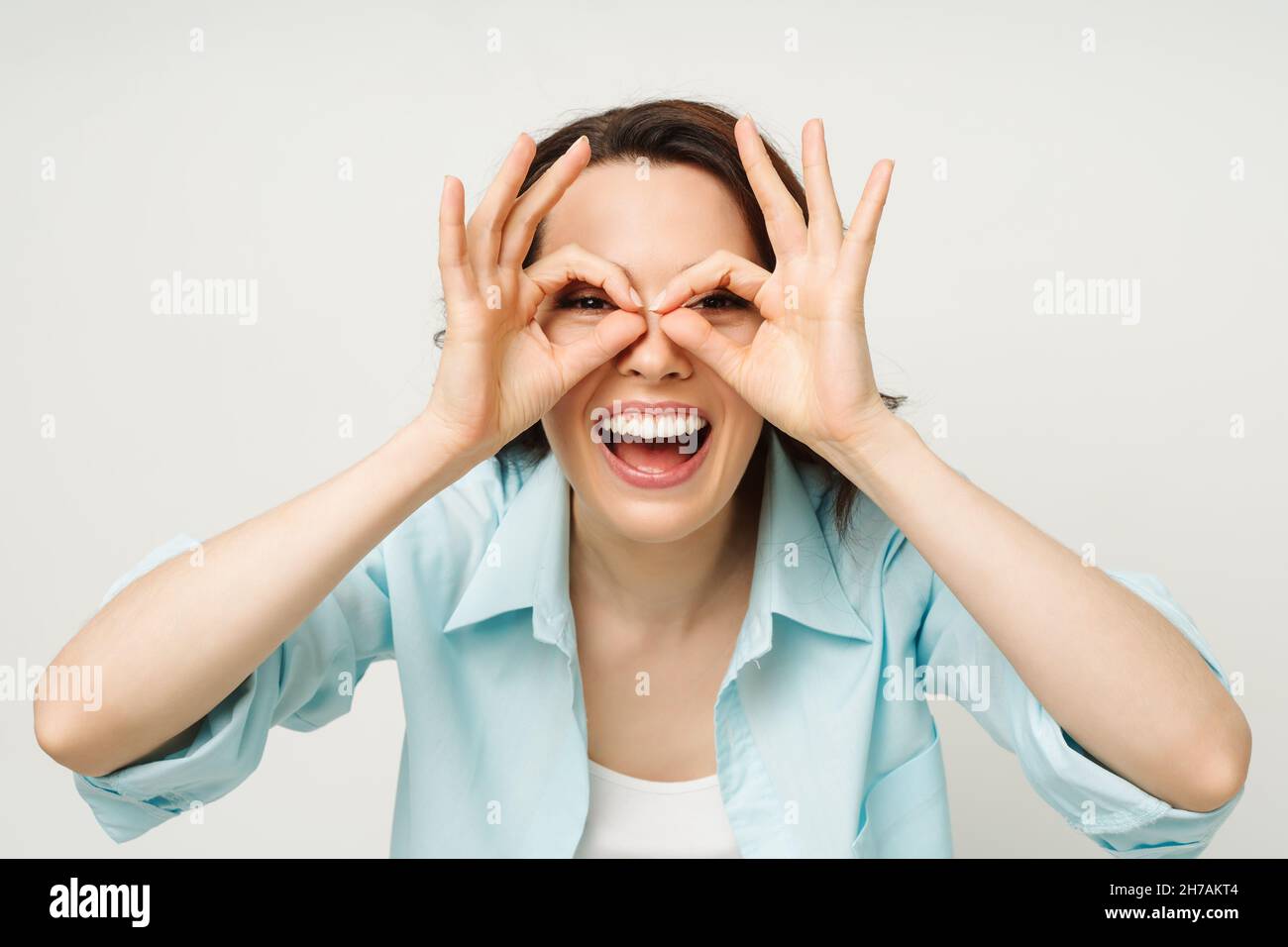 Porträt einer lächelnden Frau, die ein OK-Zeichen zeigt und in eine isolierte Kamera auf weißem Hintergrund blickt. Stockfoto