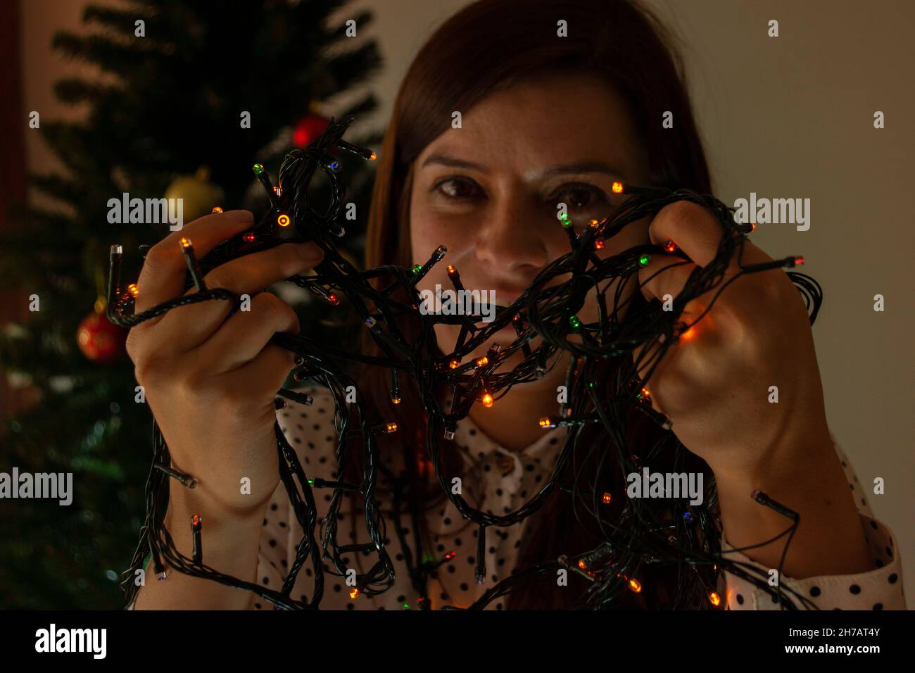 Nahaufnahme des Gesichts einer lächelnden Frau, die mit roten, grünen und blauen Lichtern spielt, um den Weihnachtsbaum in ihren Händen zu schmücken Stockfoto