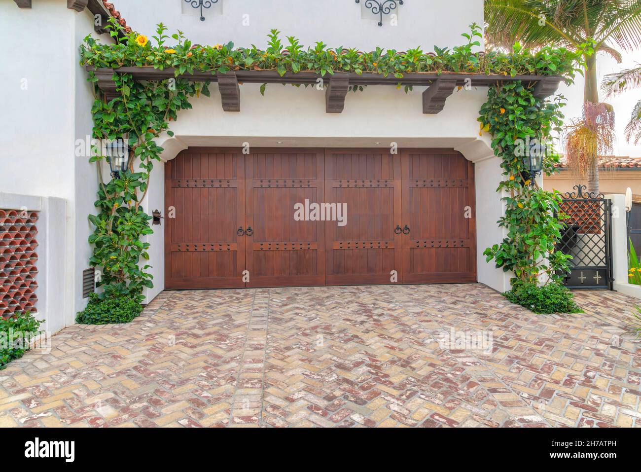 Zweifach-Garagentore aus dunklem Holz mit seitlichen Scharnieren in La Jolla, Kalifornien. Außenansicht einer Garage mit kriechenden Pflanzen auf der angeschlossenen Pergola und einer Auffahrt wi Stockfoto