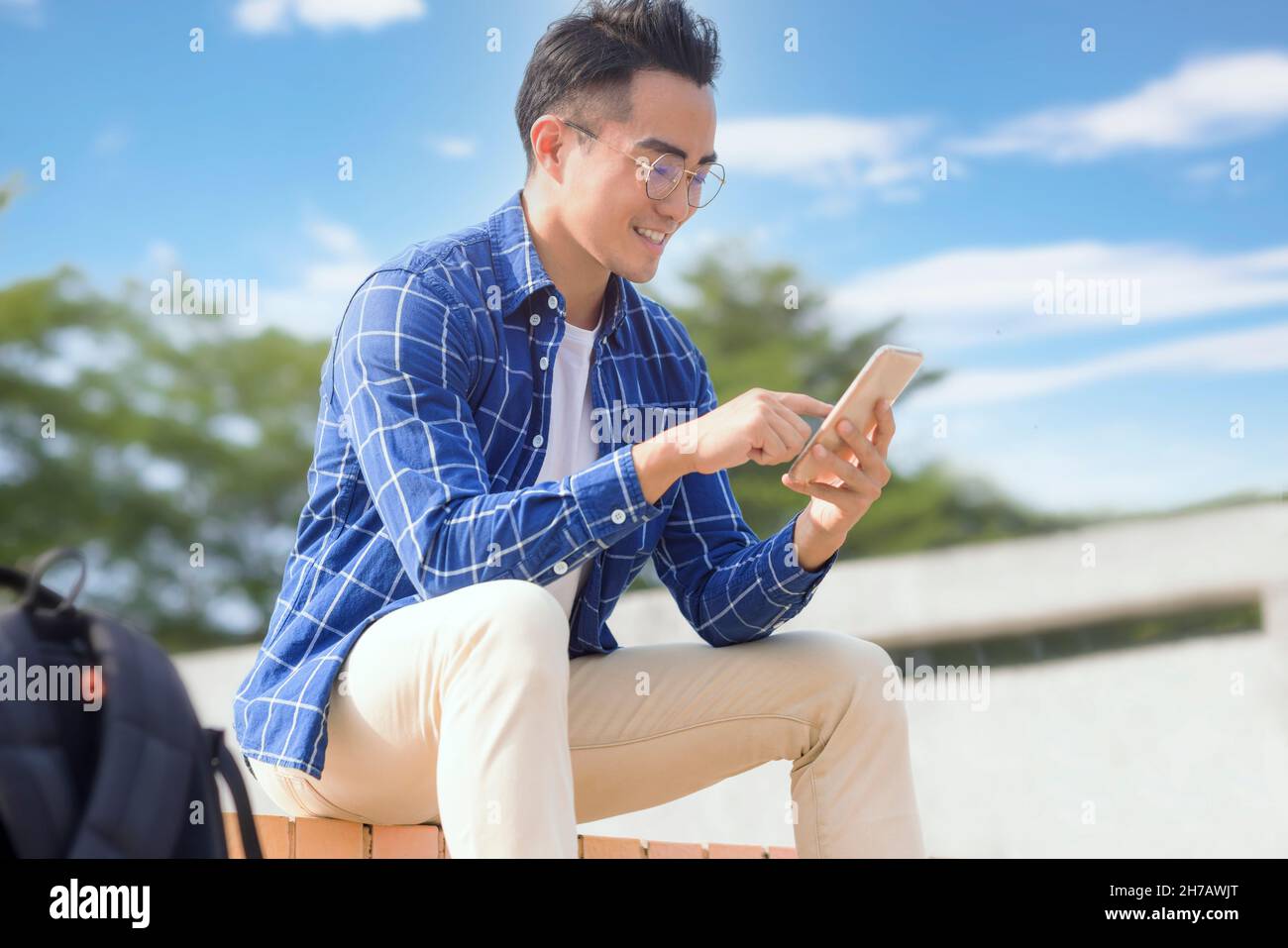 Lächelnder junger asiatischer Mann, der auf Treppen sitzt und Smartphone benutzt Stockfoto
