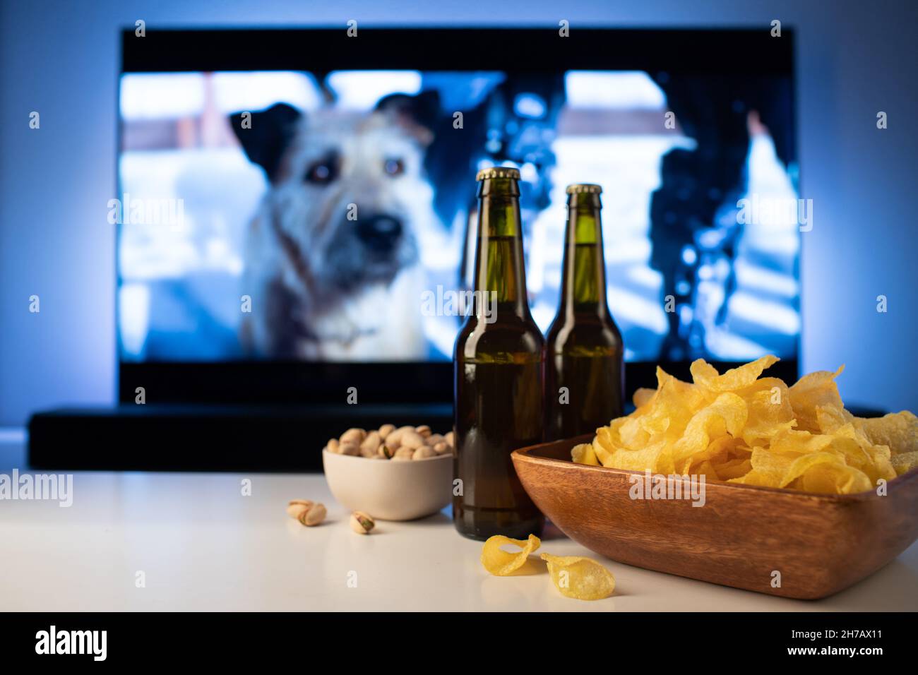 Eine Holzschüssel mit Chips und Snacks im Hintergrund funktioniert der Fernseher. Abends gemütlich einen Film oder eine Fernsehserie zu Hause mit einem Glas Bier anschauen Stockfoto