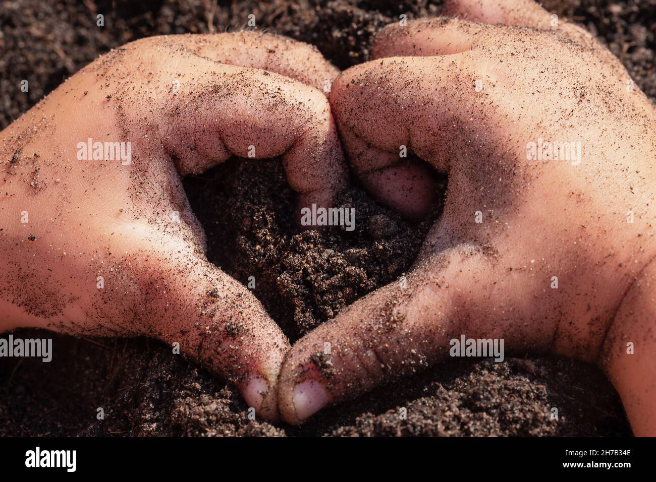 Die Hände der Kinder halten den Boden fest. Baby zeigt ein Herz aus Fingern auf dem Hintergrund der Erde Stockfoto