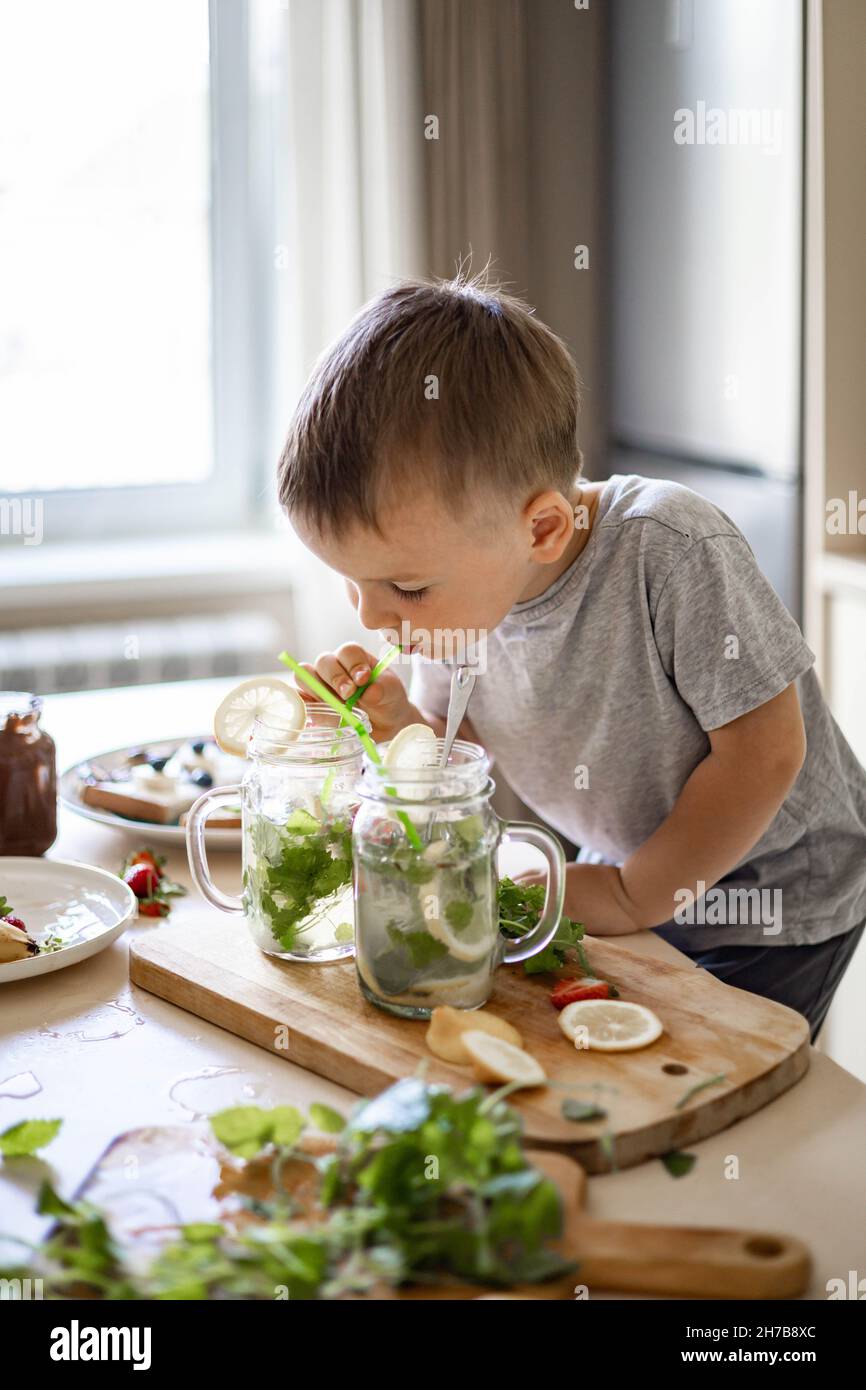 Niedlicher kleiner Junge versucht frische hausgemachte Limonade aus Glas verwenden Stroh genießen Geschmack in der modernen Küche Stockfoto