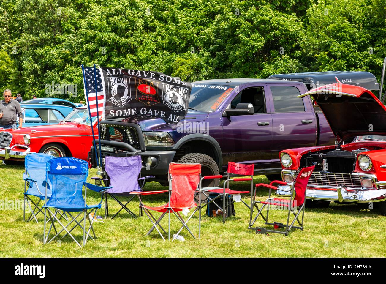 Flaggen fliegen vor einem lila Dodge RAM Pickup-Truck, der zwischen zwei Oldtimern auf einer Automshow in Fort Wayne, Indiana, USA, sitzt. Stockfoto