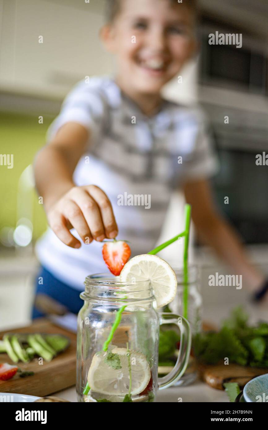 Closeup Happy Boy hinzufügen frische Erdbeerscheibe in das Glas mit hausgemachter Limonade mit Zitrone und Minze Stockfoto