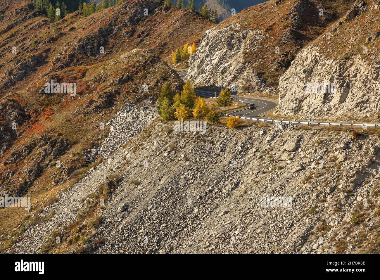 Malerischer Herbstblick auf eine kurvenreiche Asphaltstraße durch den Pass, Teil eines Bergserpentins, Felsen, Auto und goldene Bäume. Altai, Russland Stockfoto