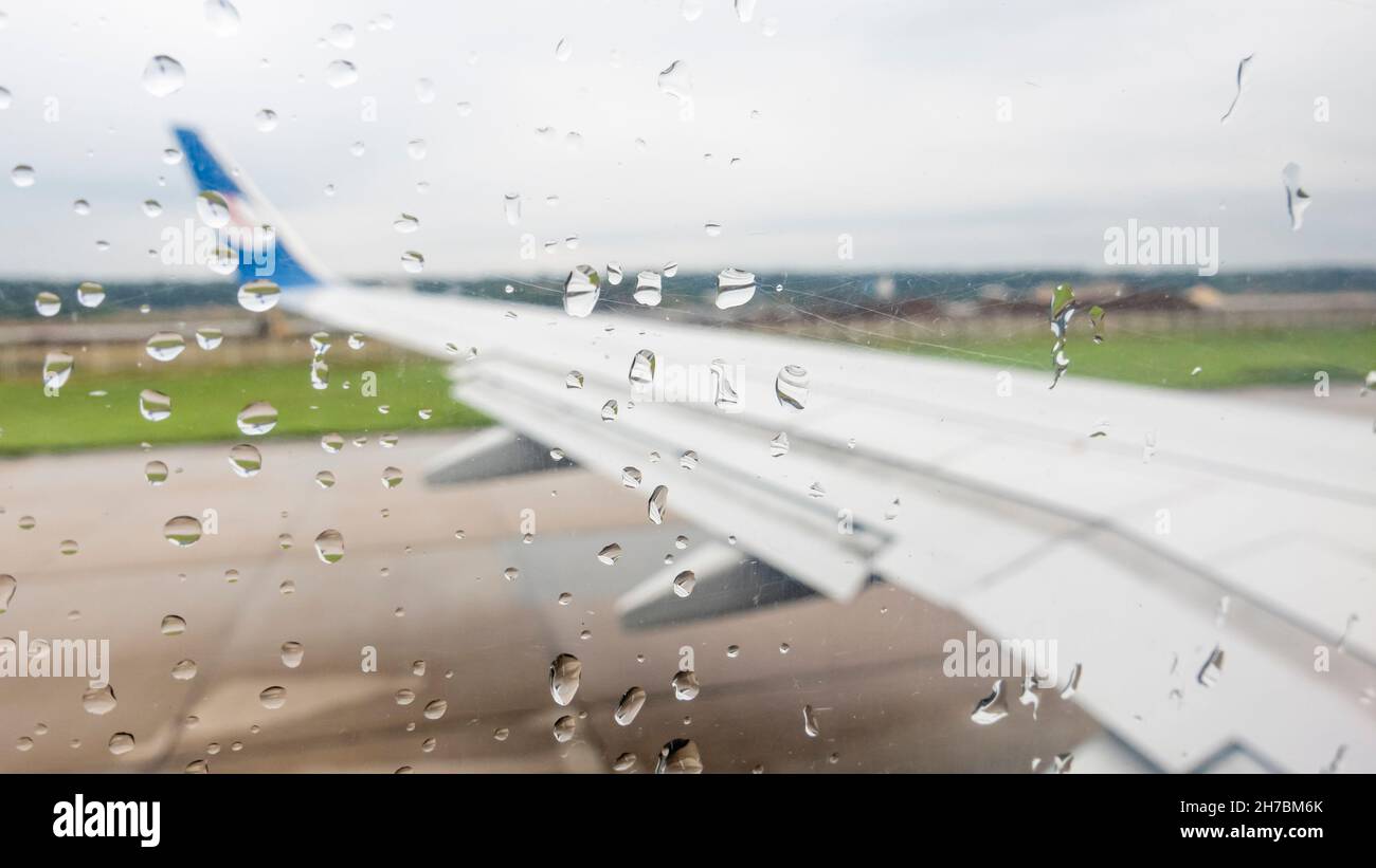 Blick auf einen Flugzeugflügel aus einem mit Wassertropfen bedeckten Fenster. Wasser tropft aus dem Flugzeugfenster von innen Stockfoto