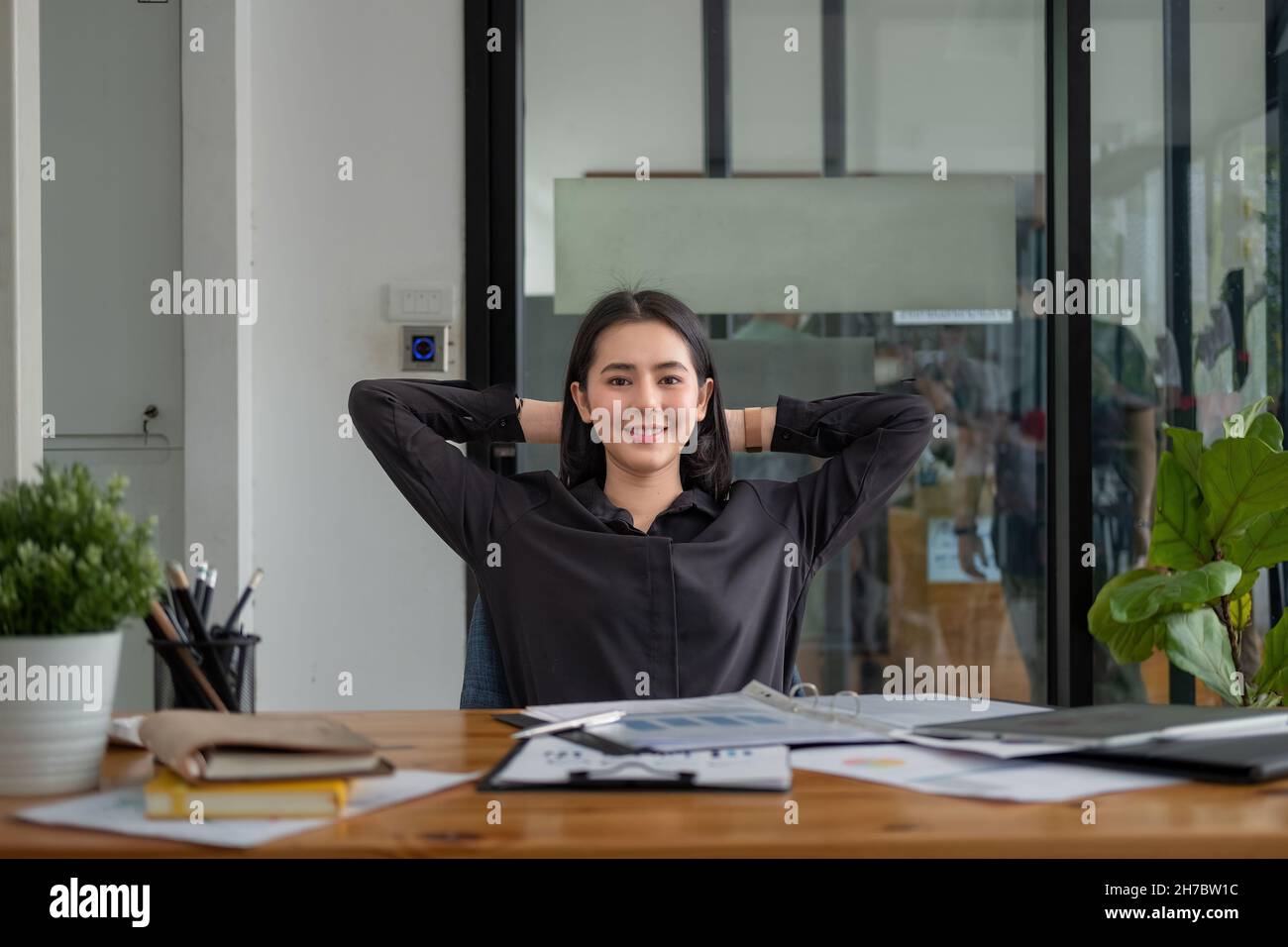 Geschäftsfrau mit Händen hinter dem Kopf, die sich in der Pause in einem bequemen Bürostuhl entspannt. Lächelnde asiatische Angestellte, die sich nach der Arbeit ausruhte und sich lehnte Stockfoto