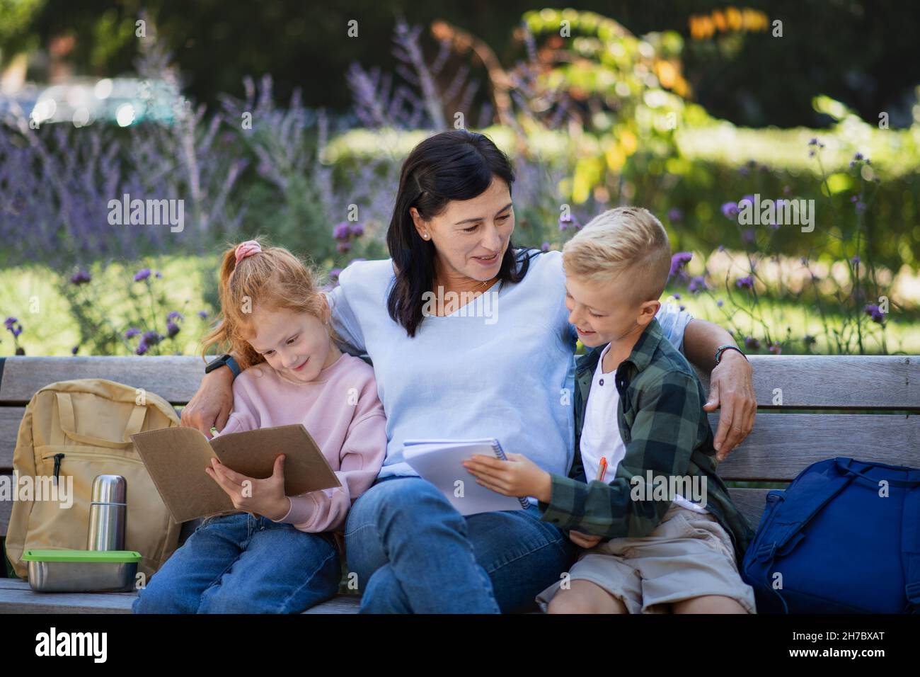 Glückliche ältere Frau mit Enkelkindern, die auf der Bank sitzen und bei Hausaufgaben im Park helfen. Stockfoto