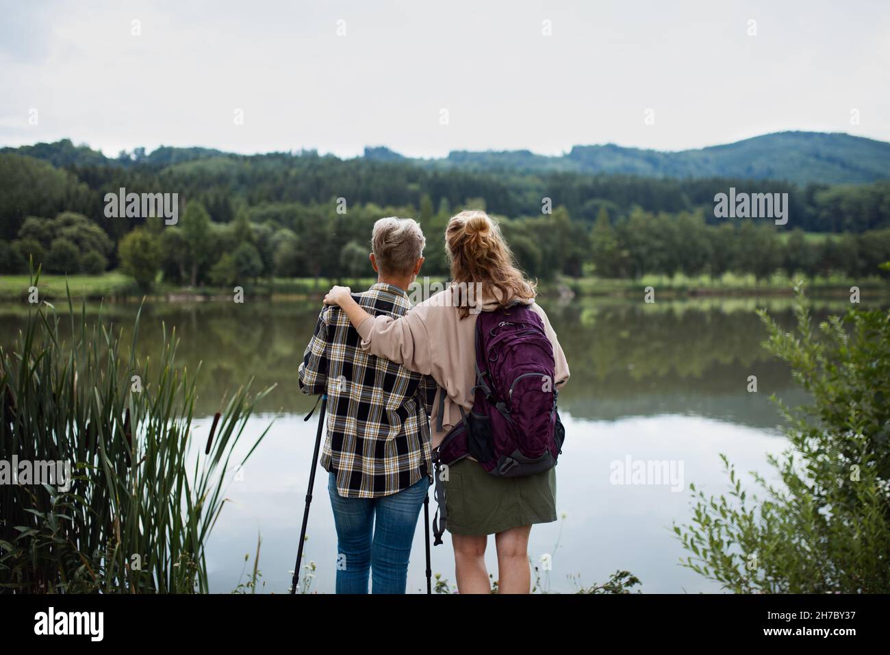 Rückansicht der älteren Mutter, die sich mit der erwachsenen Tochter umarmt, wenn sie im Freien am See in der Natur steht Stockfoto