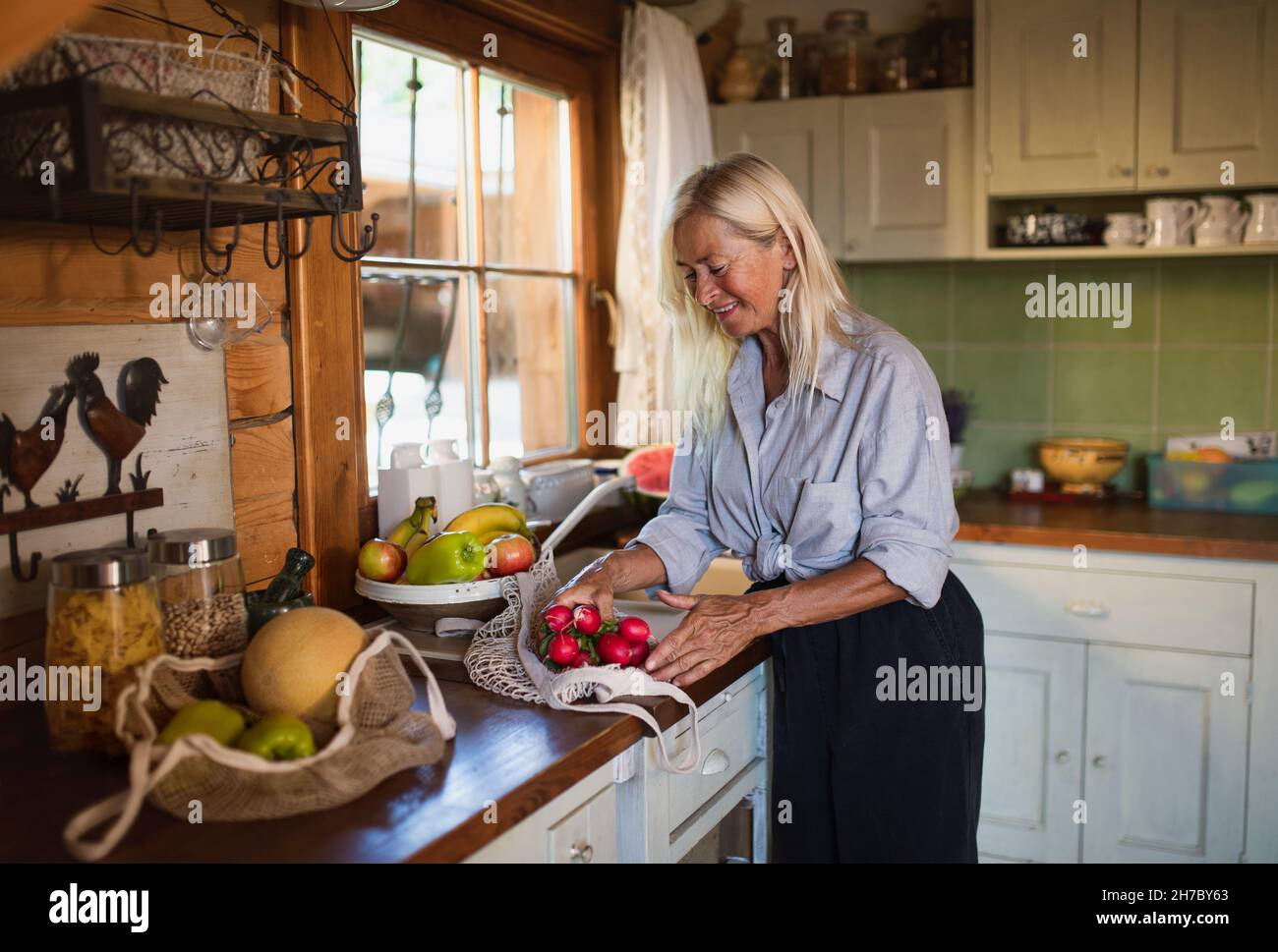 Glückliche ältere Frau beim Auspacken von Geschäften zuhause, nachhaltiger Lebensstil. Stockfoto