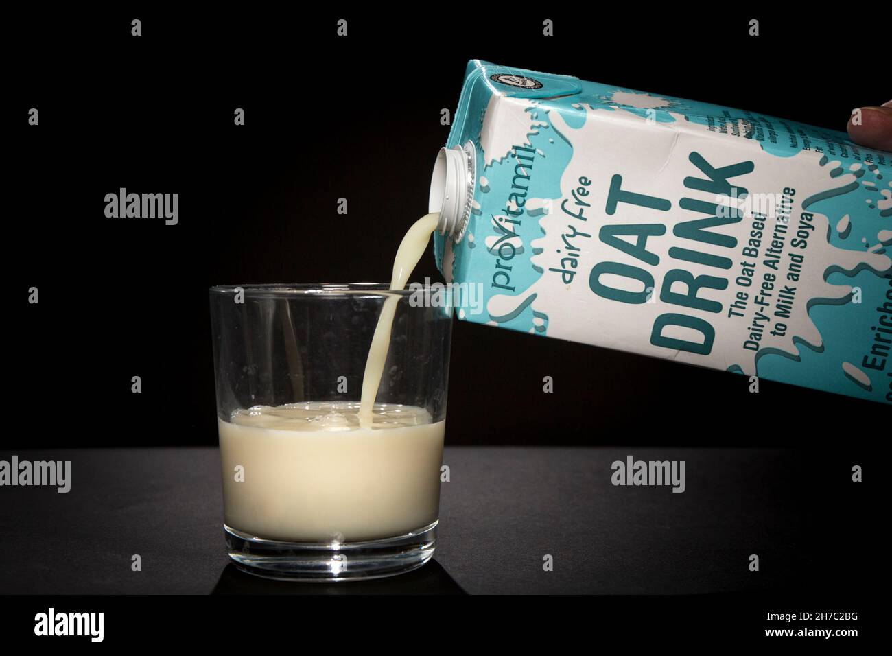 Milchfreier Hafer trinkt Milch, die aus einem Karton in ein Glas gegossen wird. Stockfoto
