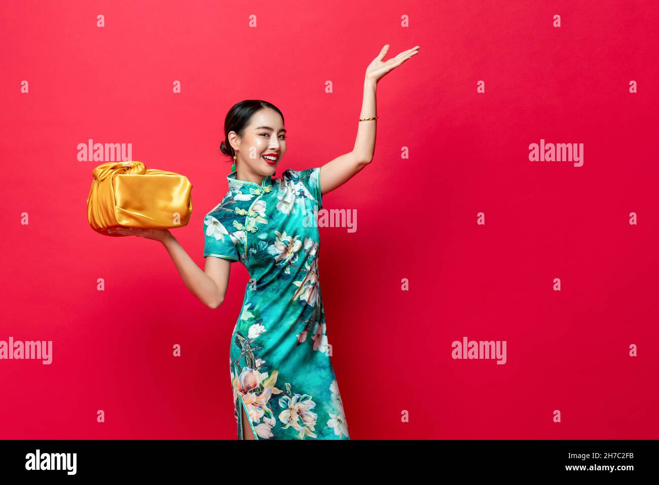Lächelnde hübsche asiatische Frau im orientalischen Stil Kostüm mit goldener Geschenkbox in rot isoliertem Studiohintergrund für chinesische Neujahrskonzepte Stockfoto