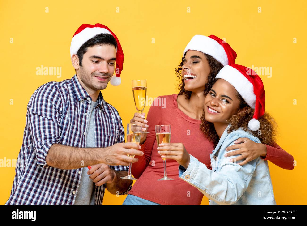 Glückliche, vielfältige Freunde trinken Champagner und feiern Weihnachten auf einem isolierten gelben Studiohintergrund Stockfoto
