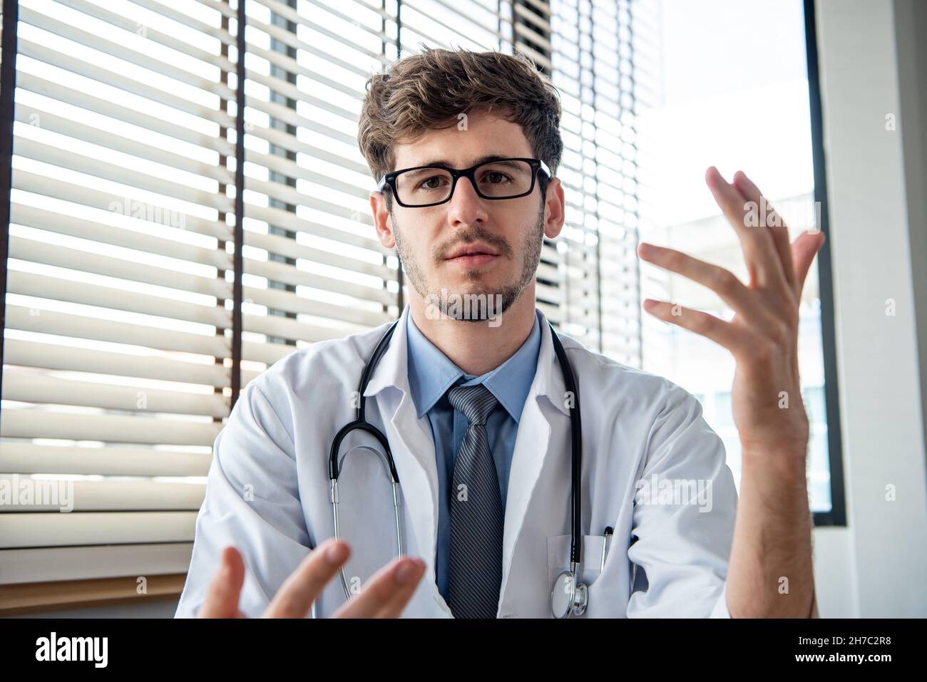 Junger männlicher Arzt, der Kamera ansieht und erklärt, medizinische Fernberatung oder telemedizinische Konzepte Stockfoto
