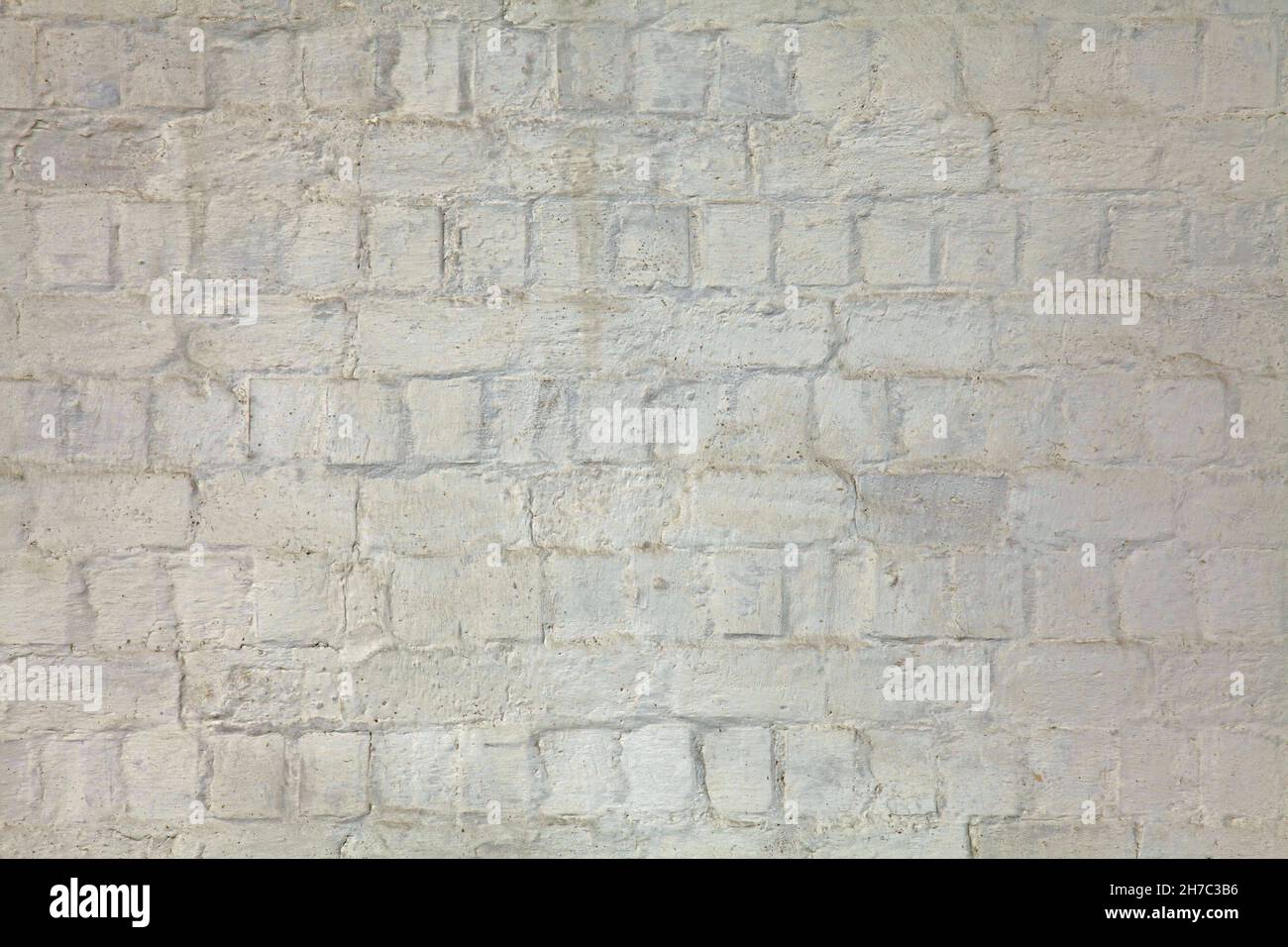 Weiße und unebene weiß getünchte Wand, Textur, Hintergrund. Alte Gebäudewand, bemalt mit Wittling. Wellige, holprige, struppige Oberfläche Stockfoto