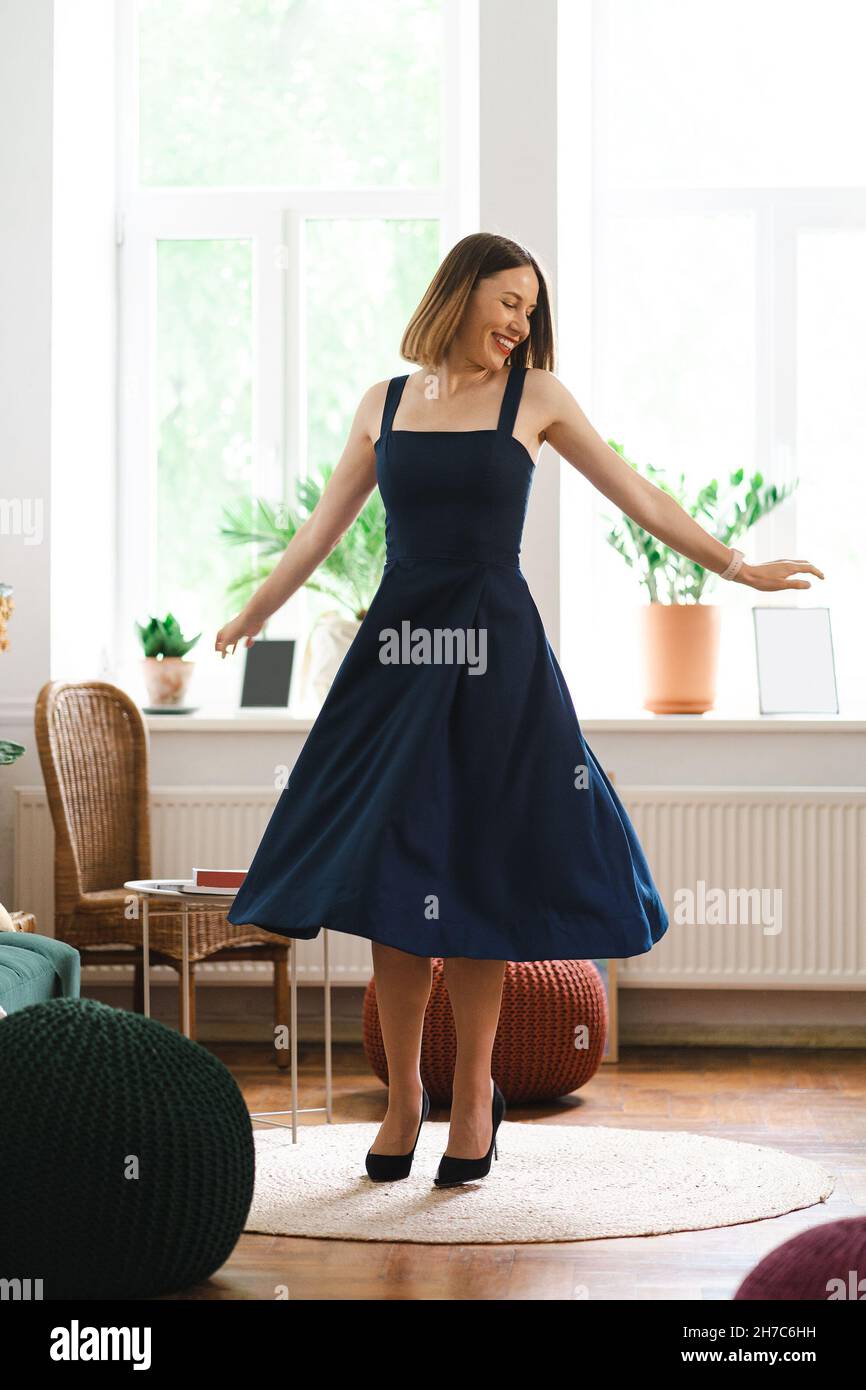 Schöne Frau trägt ein langes marineblaues Kleid und hohe Hügel Schuhe, die Spaß zu Hause tanzen, lächeln. Sie feiert glücklich den Erfolg Stockfoto