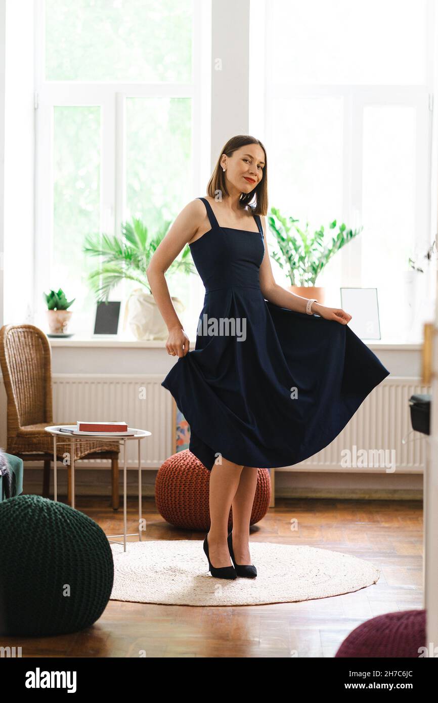 Schöne Frau trägt ein langes marineblaues Kleid und hohe Hügel Schuhe, die Spaß zu Hause tanzen, lächeln. Sie feiert glücklich den Erfolg Stockfoto