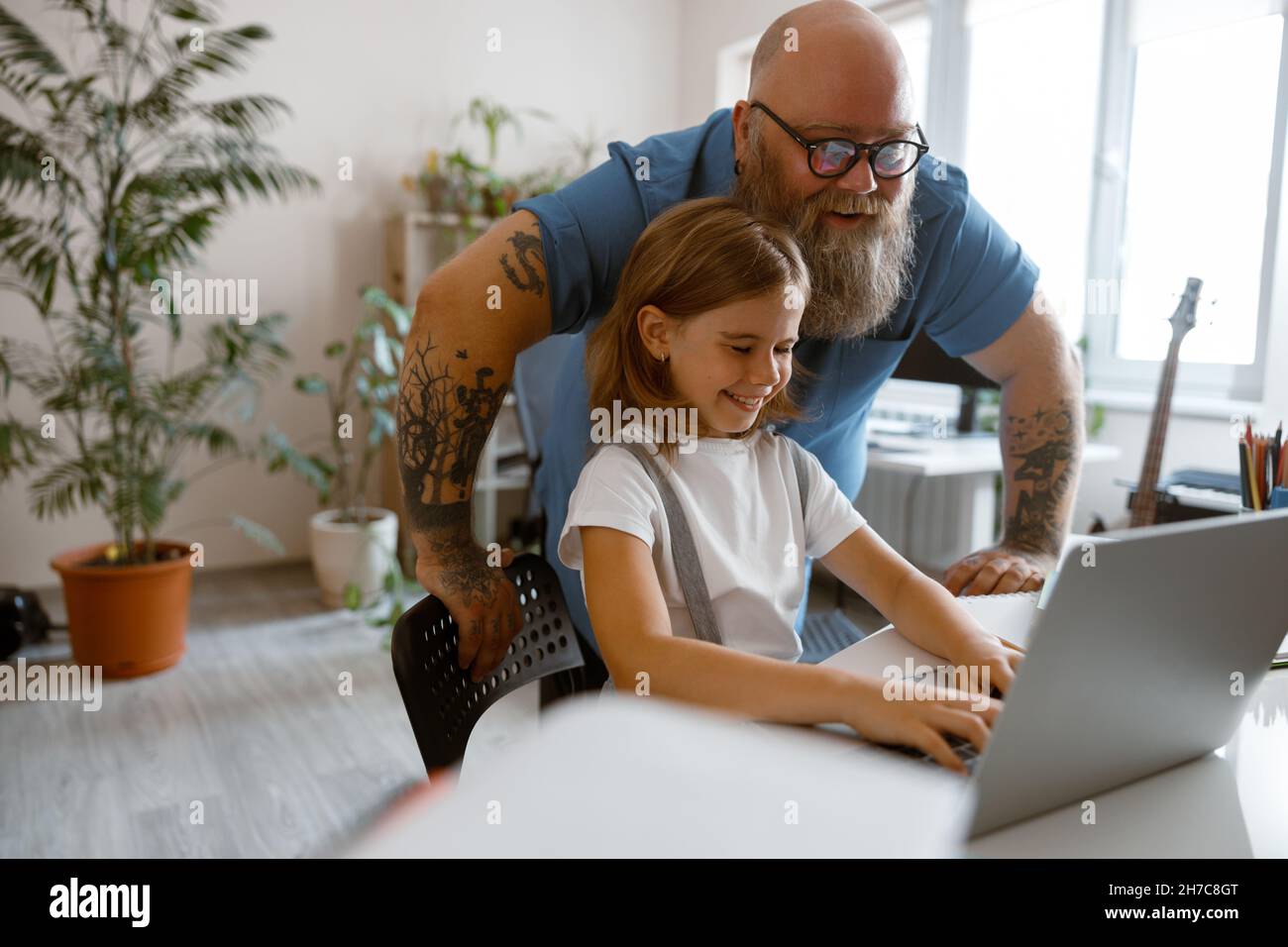 Ein glücklicher Vater mit einem kleinen Mädchen macht am Tisch im Zimmer eine Hausfrau auf einem modernen Laptop Stockfoto