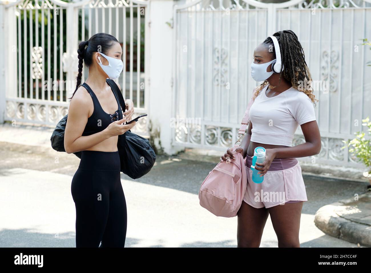 Junge Freundinnen in medizinischen Masken treffen sich im Freien, um gemeinsam ins Fitnessstudio zu gehen Stockfoto